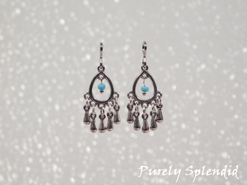 Silver colored open teardrop shaped earrings with five silver colored drops hanging below and one blue colored bead hanging in the center of the teardrop.