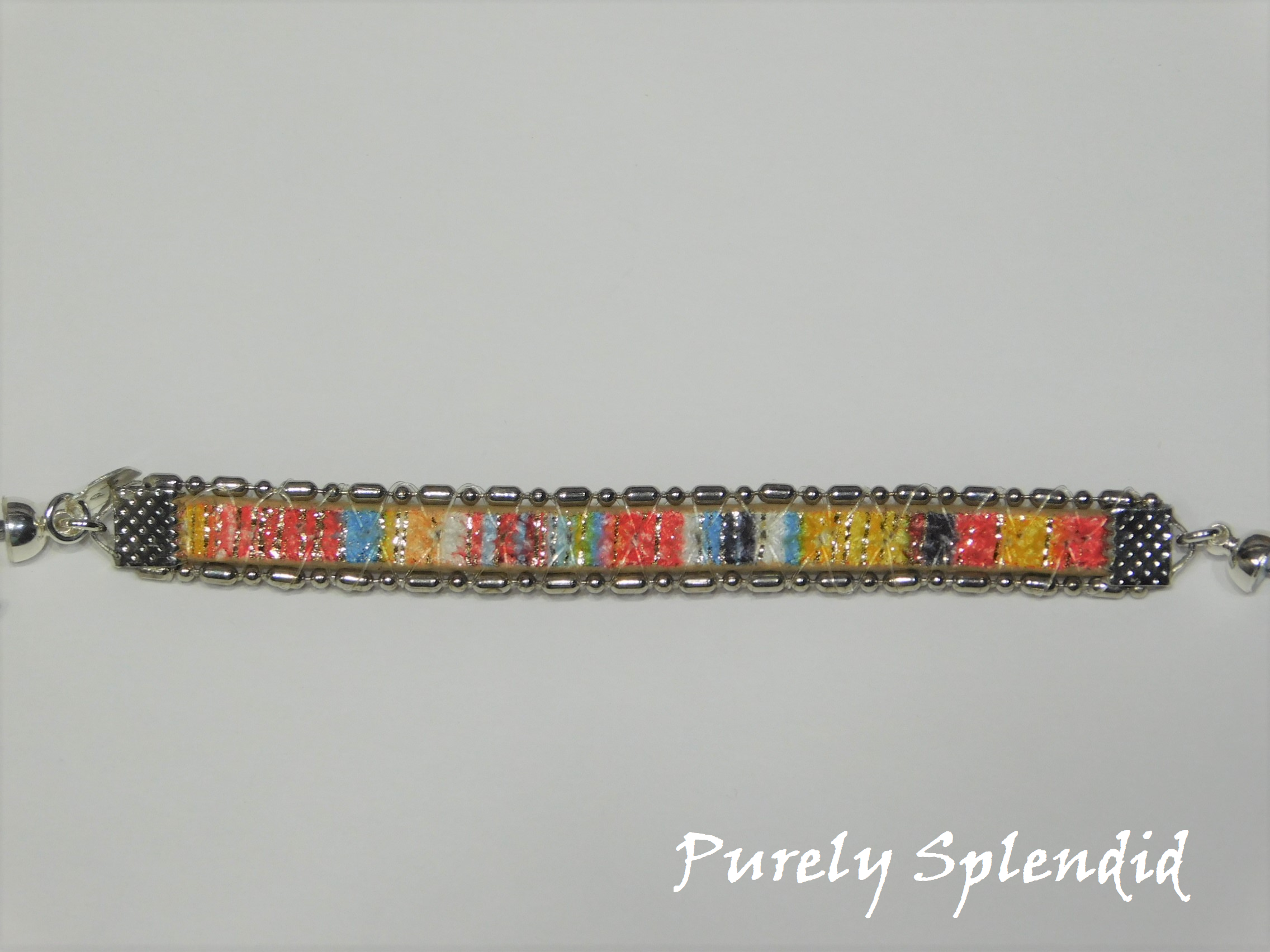 Full picture of the Southwestern Sunset Bracelet. Beautiful striped pattern of yellows, orange, blue, red, white with some sparkling threads, edged with a silver chain. Created for doll who have a 3 1/4" wrist. Closes with a magnetic clasp.