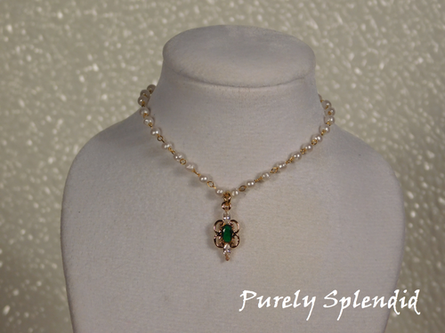 Dainty pearl like beads are part of a gold chain. Focal point is an Emerald cubic zirconia pendant hanging from the pearl chain.
