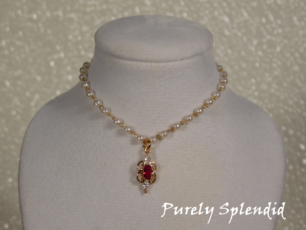 Dainty pearl like beads are part of a gold chain. Focal point is a Ruby cubic zirconia pendant hanging from the pearl chain.
