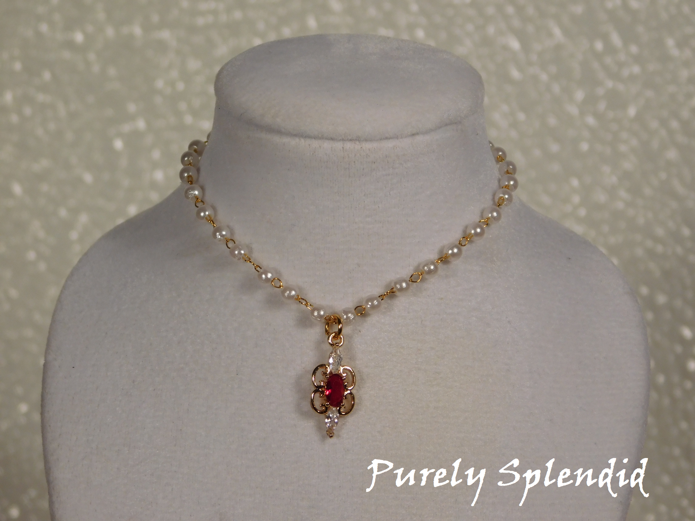 Dainty pearl like beads are part of a gold chain. Focal point is a Ruby cubic zirconia pendant hanging from the pearl chain.