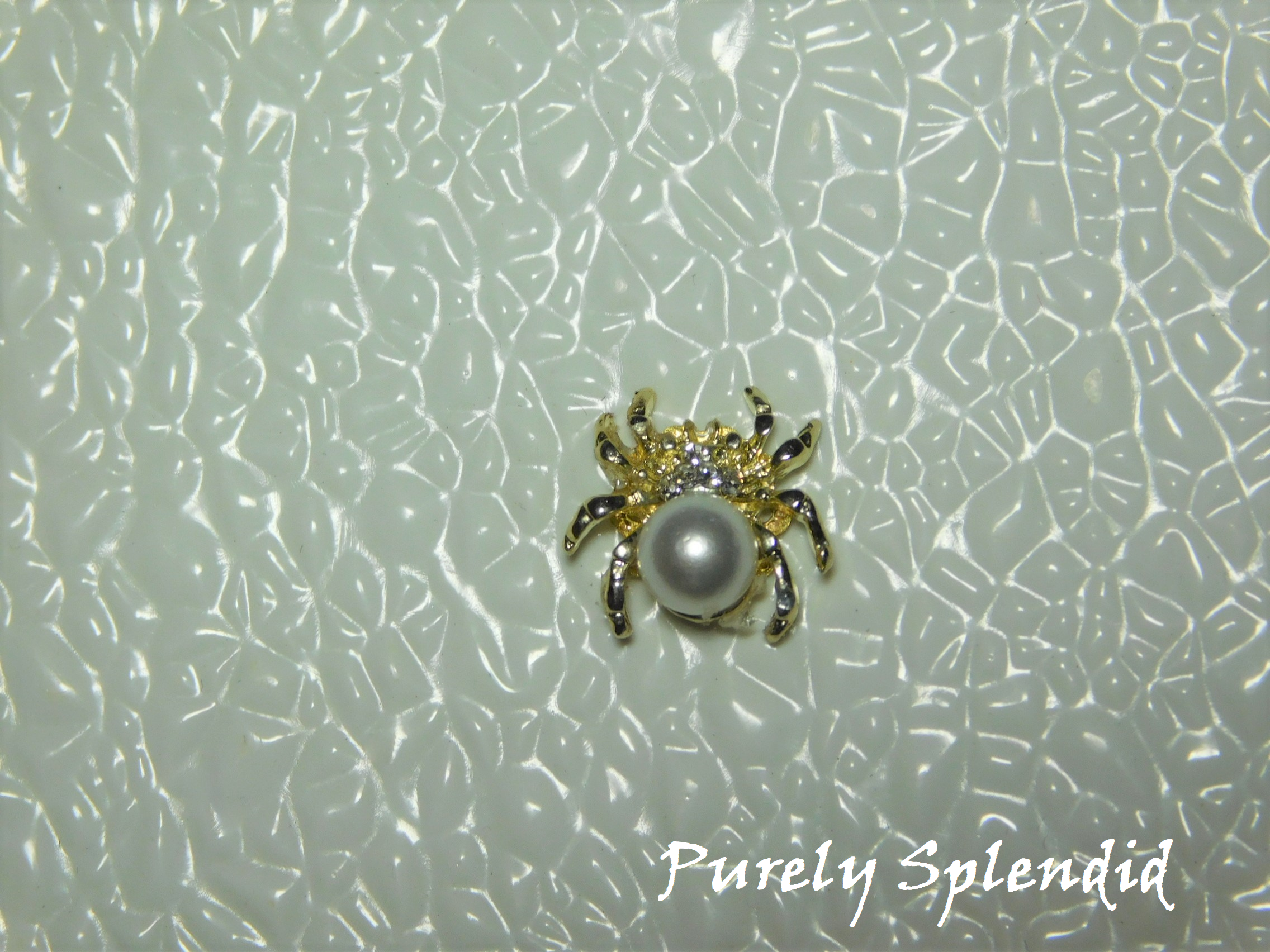 A large faux pearl makes up the body of this Spider Brooch.