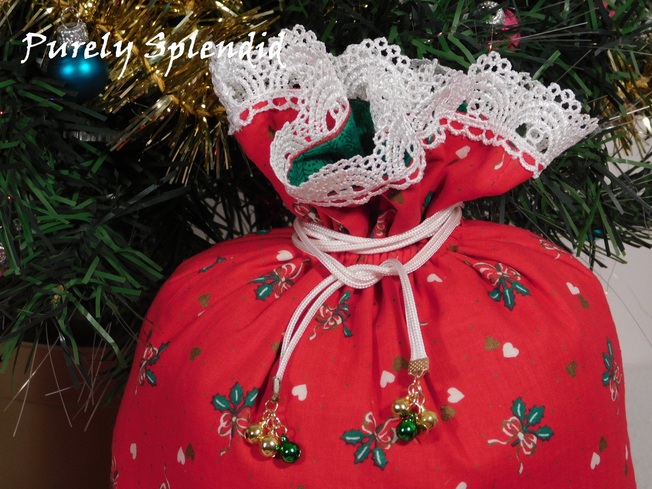 close up of the pretty white lace edging the top of the gift bag and the white drawstrings with 3 small jingle bells hanging from each end of the drawstring
