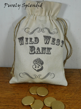 Load image into Gallery viewer, handmade beige canvas double drawstring bag with the words Wild West Bank $ printed on the front. Shown with 6 golden wooden coins
